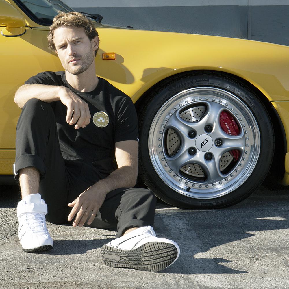 Man wearing black oloi tee next to a yellow racecar