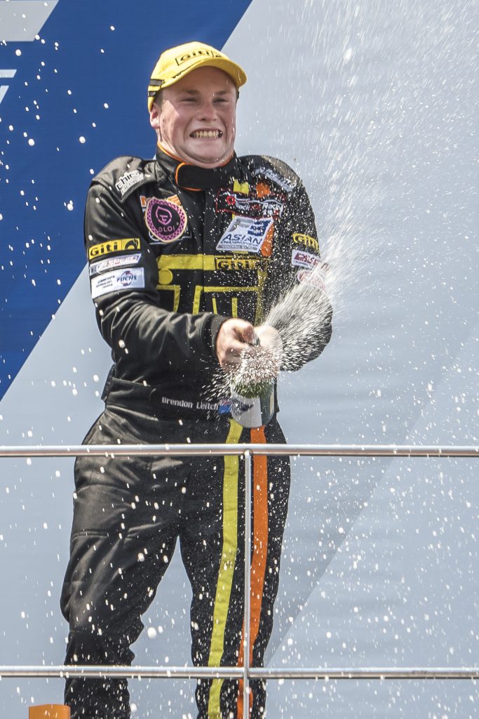 Driver Brendon Leitch sprays champagne from atop the winners' podium